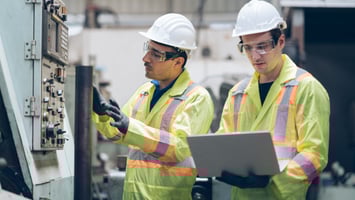 Image of two men in hard hards, safety vests, and goggles, working 