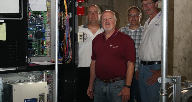 Image of four men standing behind an AC elevator drive