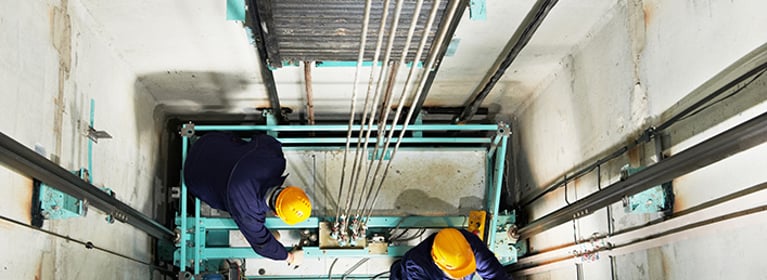 Two certified elevator technicians performing maintenance or adjustments.