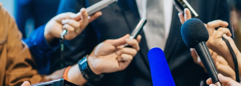 Image of Man in Suit surrounded by Microphones