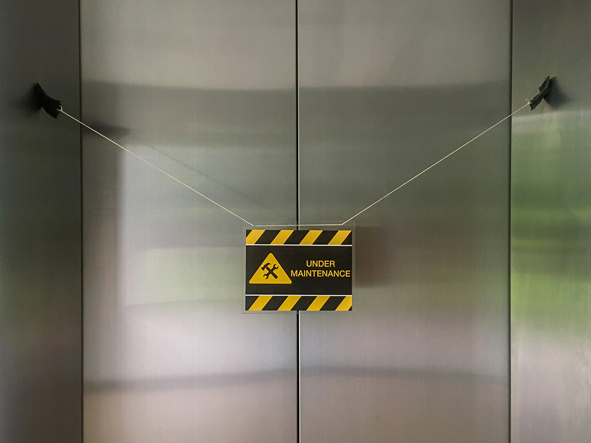Closed elevator door with a &ldquo;Under Maintenance&rdquo; warning sign hanging across the doors